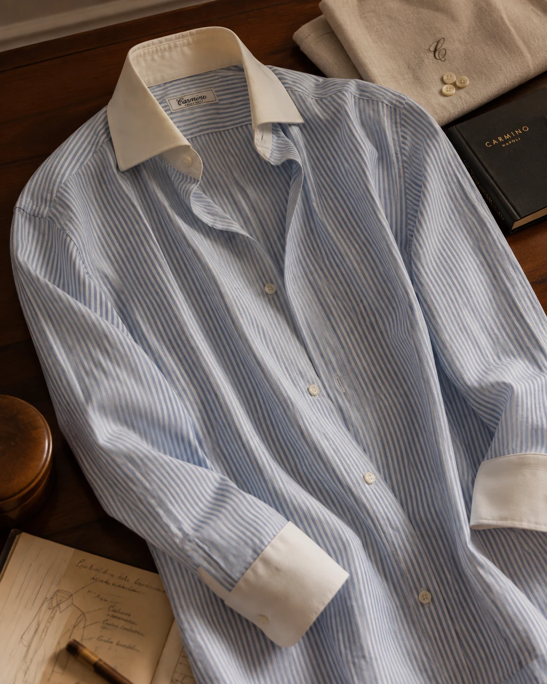 Chemise Carmino rayée bleu et blanc présentée sur une table en bois dans un univers sartorial